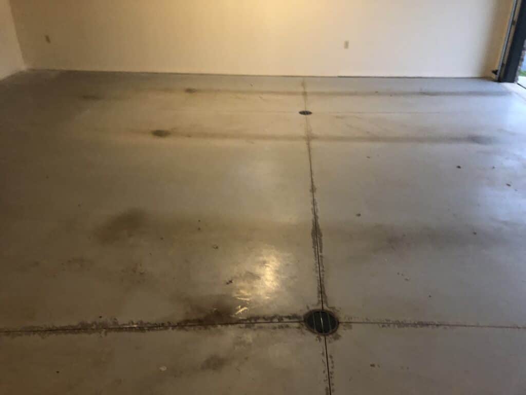 An empty room with a concrete floor showing stains and a drain in the center. Walls appear unfinished, with no baseboards, suggesting a utility space.